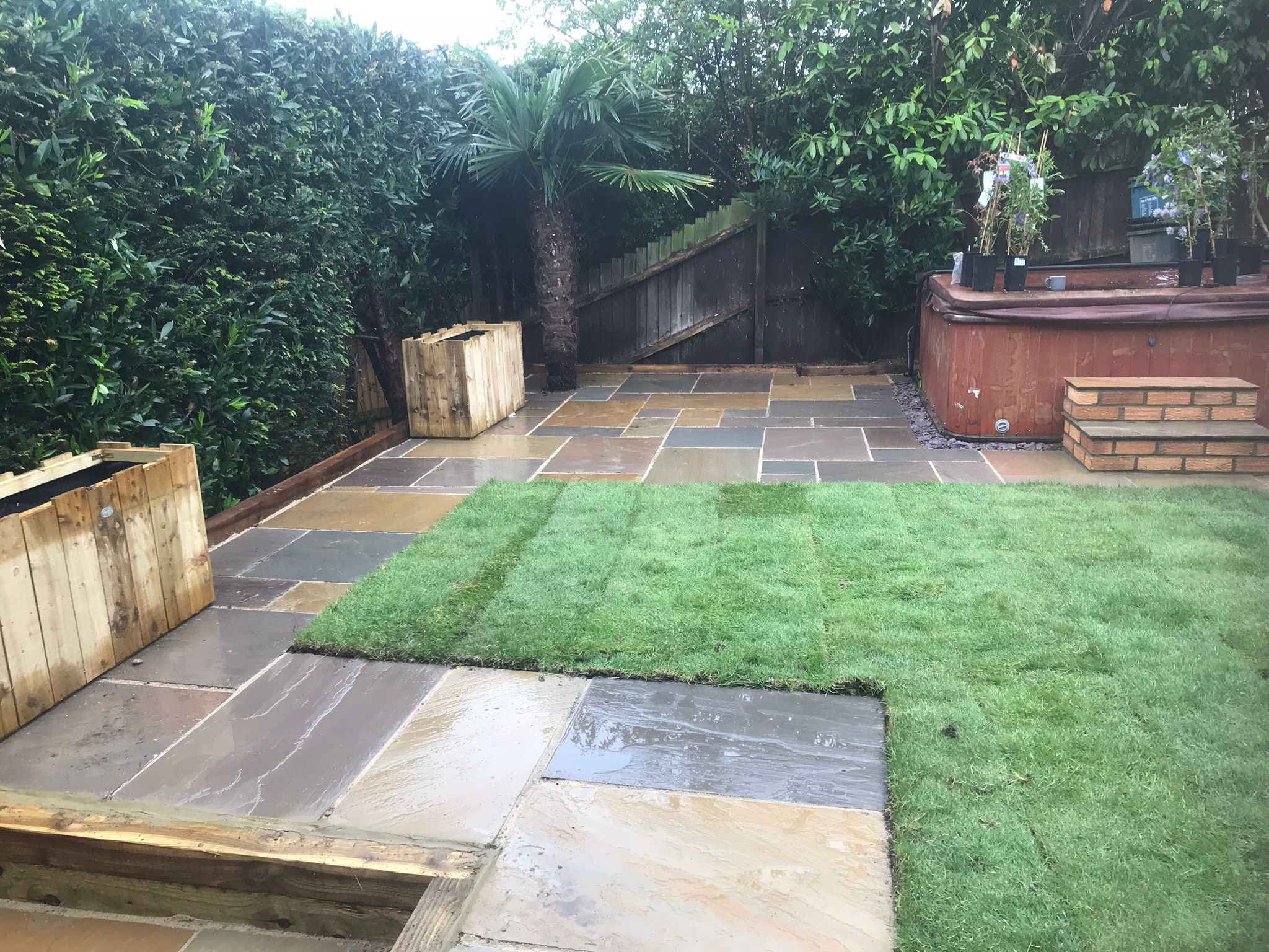 This is a photo of newly installed Indian Sandstone paving slab patio and walk way in a residential garden.